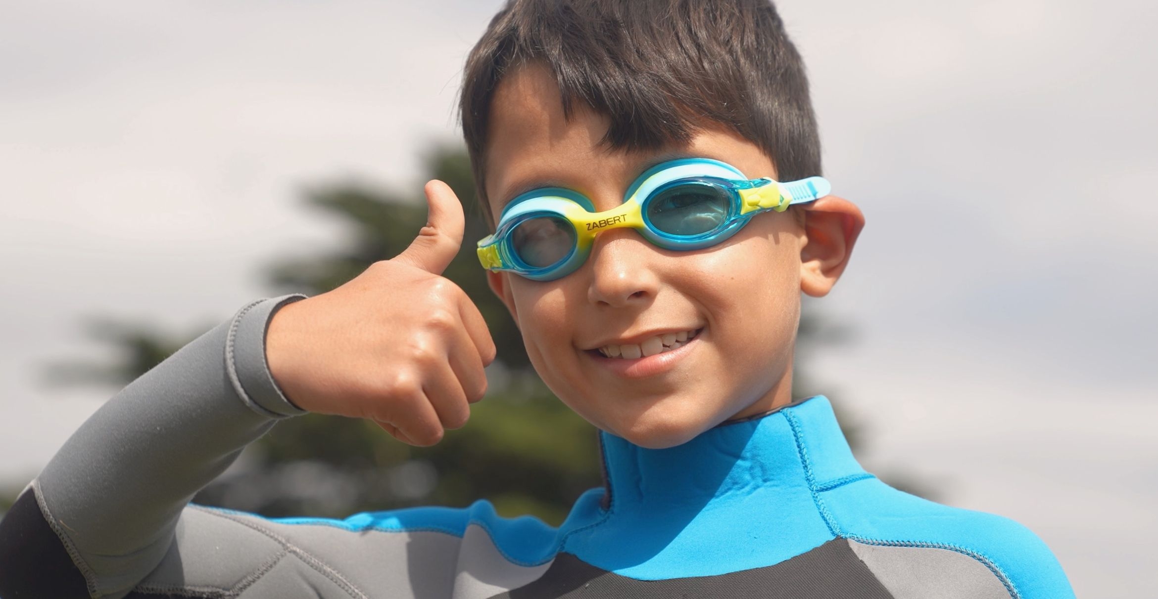 a boy in a wetsuit and swim goggles give a thumbs-up