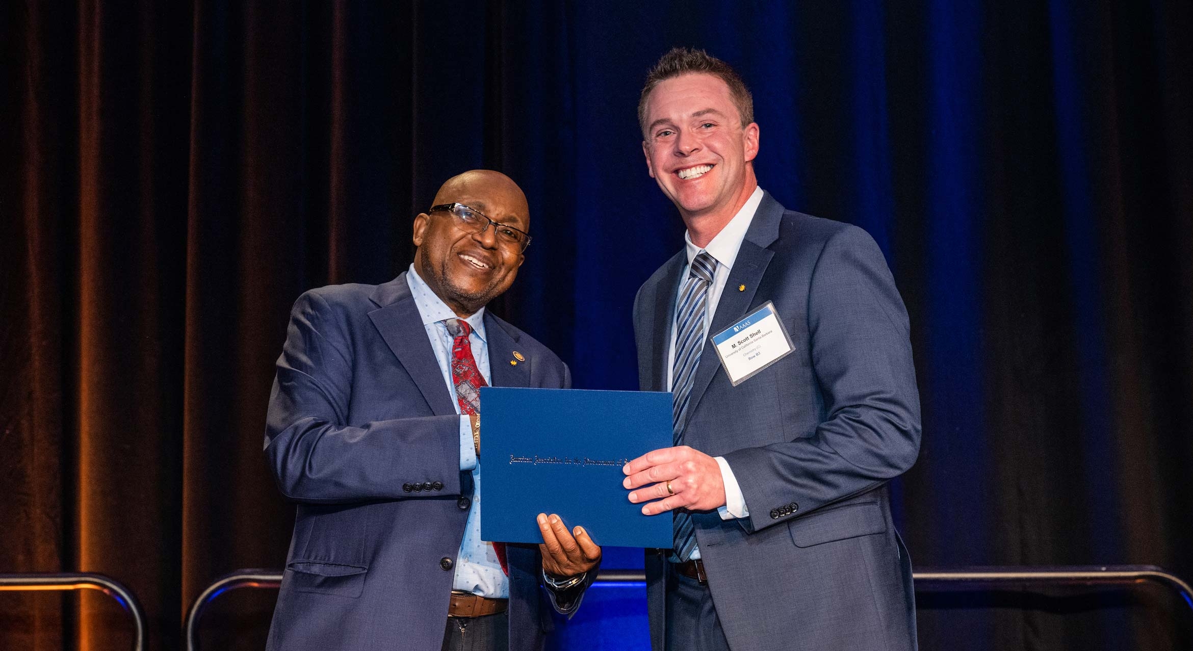 Black man hands blue card to white man on stage