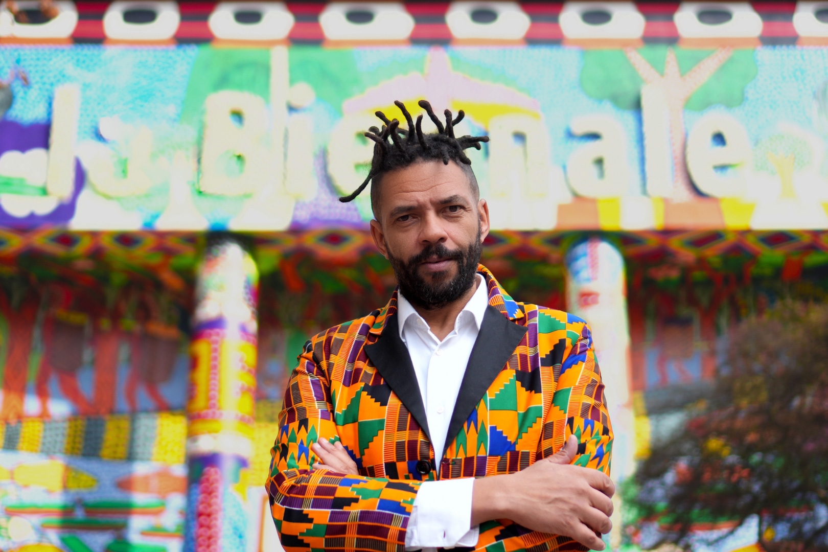 Black man in blazer with African colors in front of colorful artistic backdrop saying Bienale