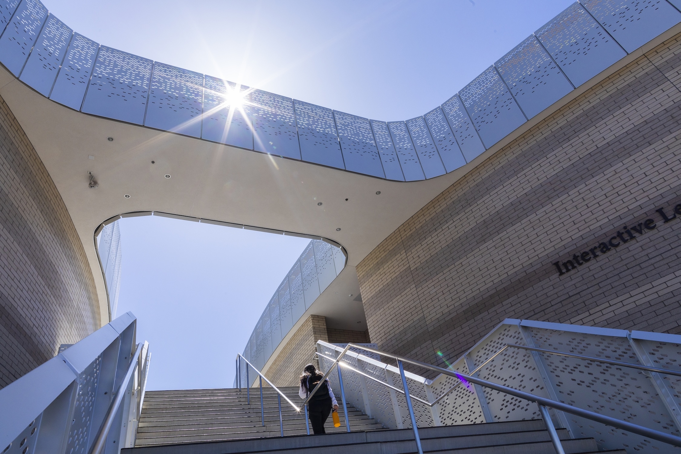 One person ascending outdoor stairs of a modern building with a sunburst overhead