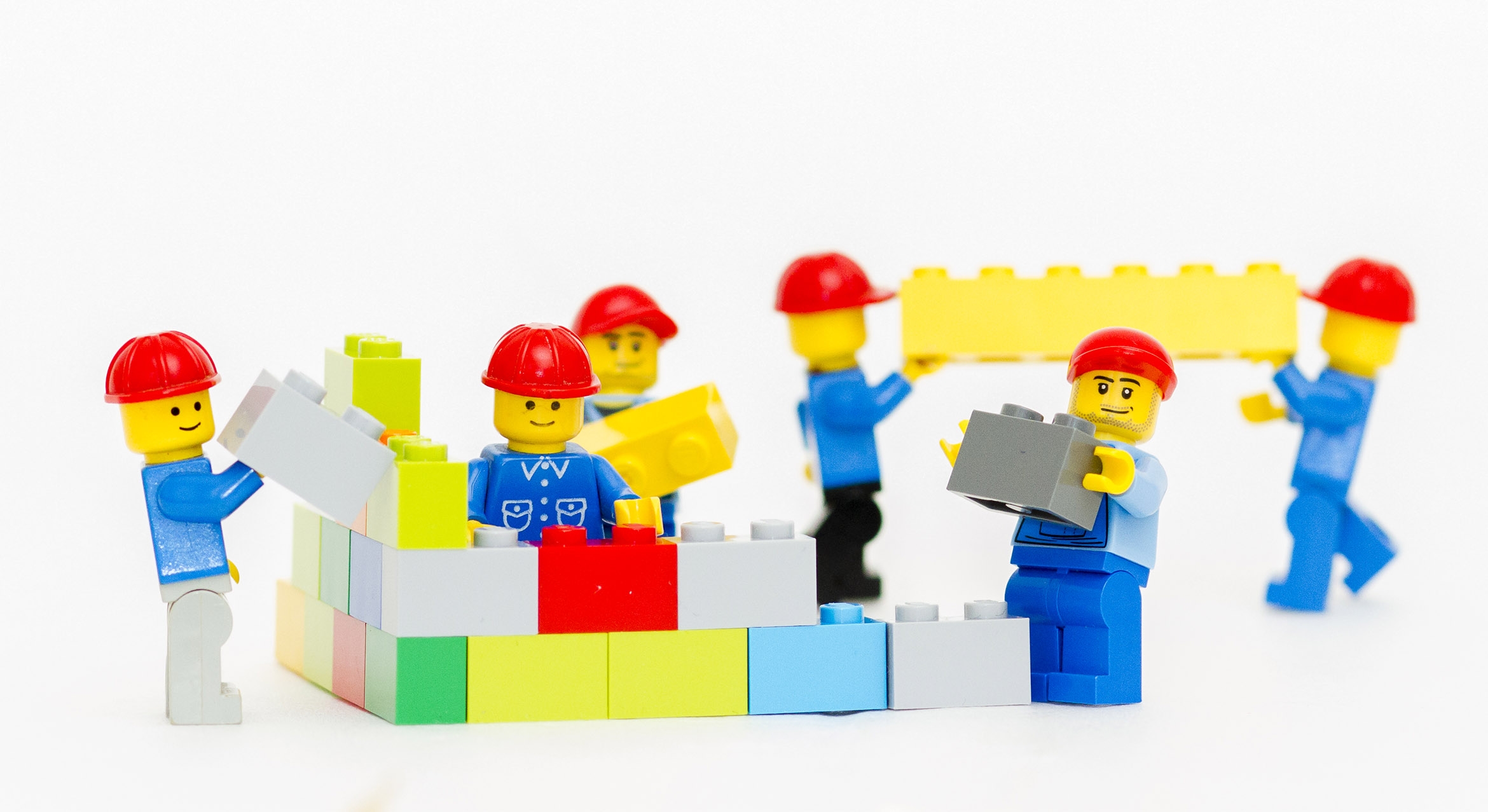 Lego mini figures in red construction hats building a structure using Lego bricks