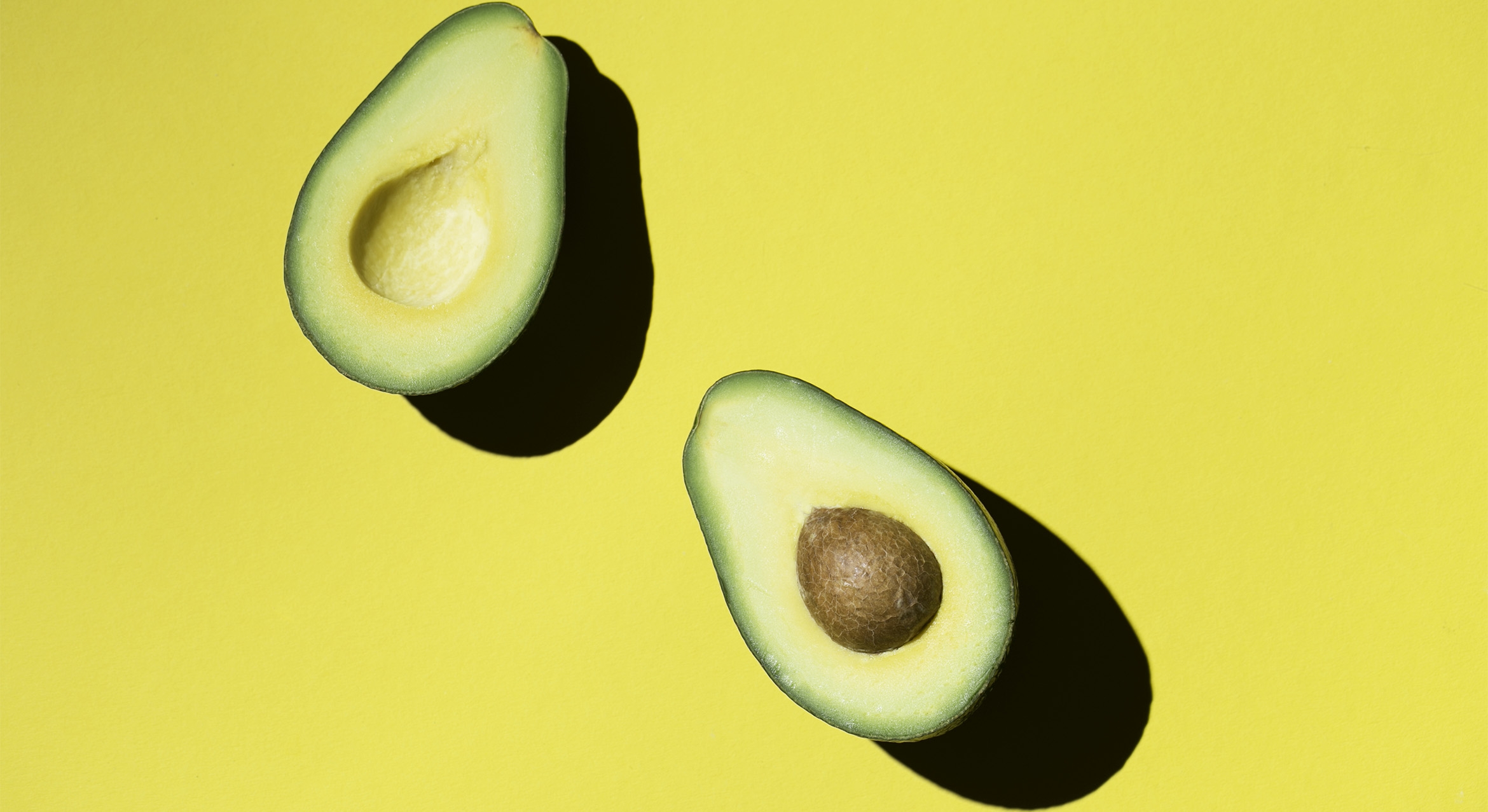 An avocado cut in half displayed on a yellow background