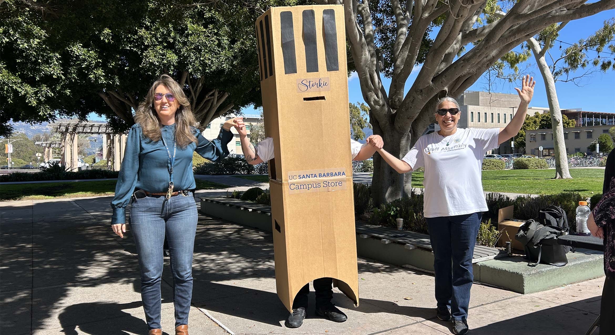 Two women hold hands with a man dressed as Storke Tower.