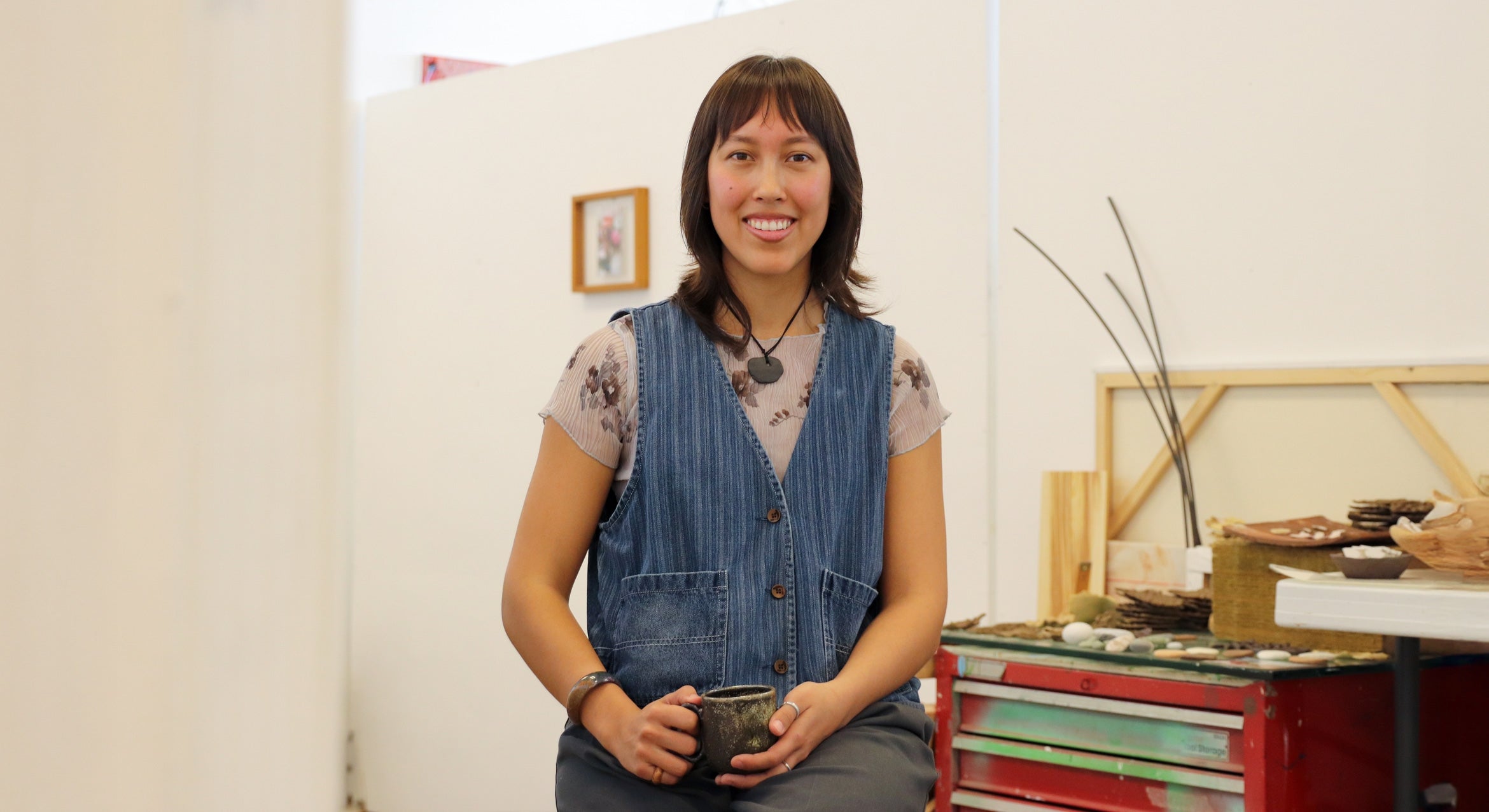 college age woman of Taiwanese descent sits in studio with branches and canvas