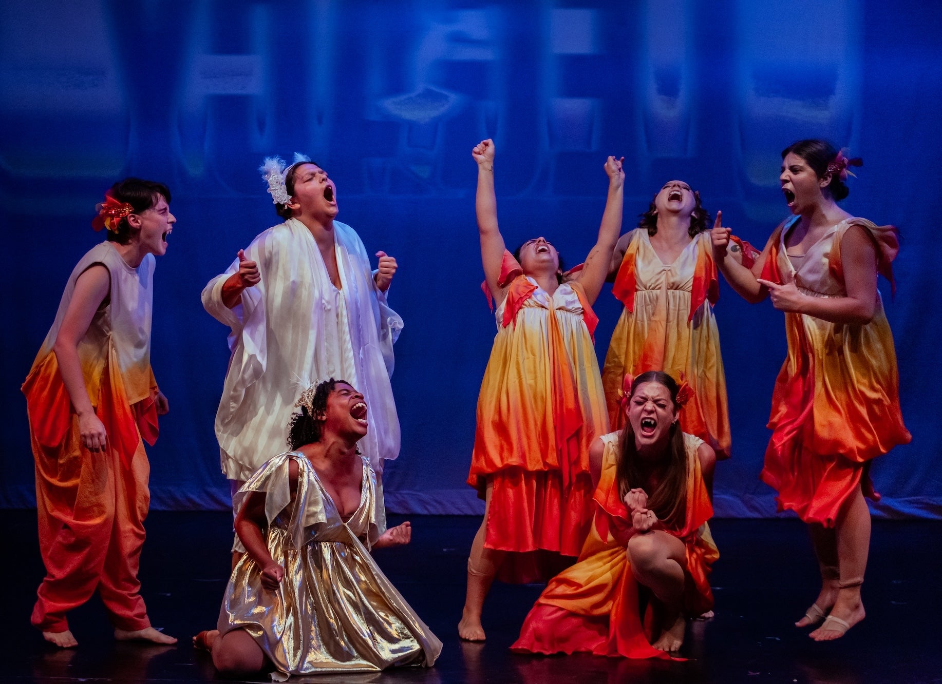 Women in bright colored dresses on stage with a blue background