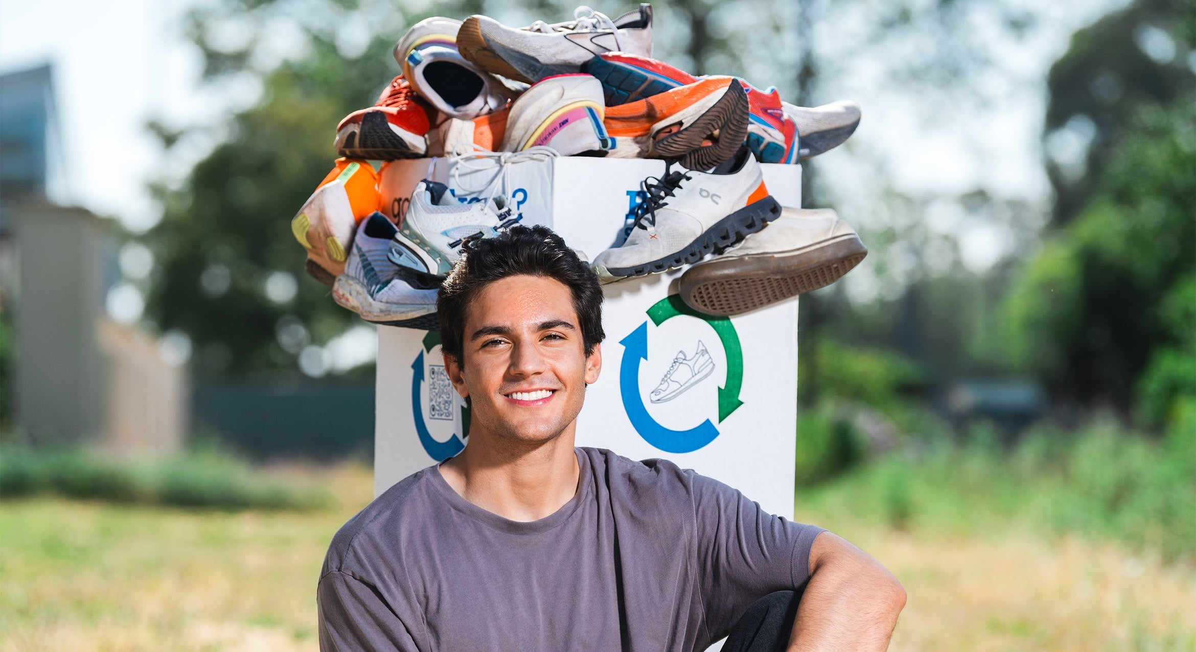 color photograph of student Matthew Schoen sitting next to shoe donation box overflowing with old sneakers 