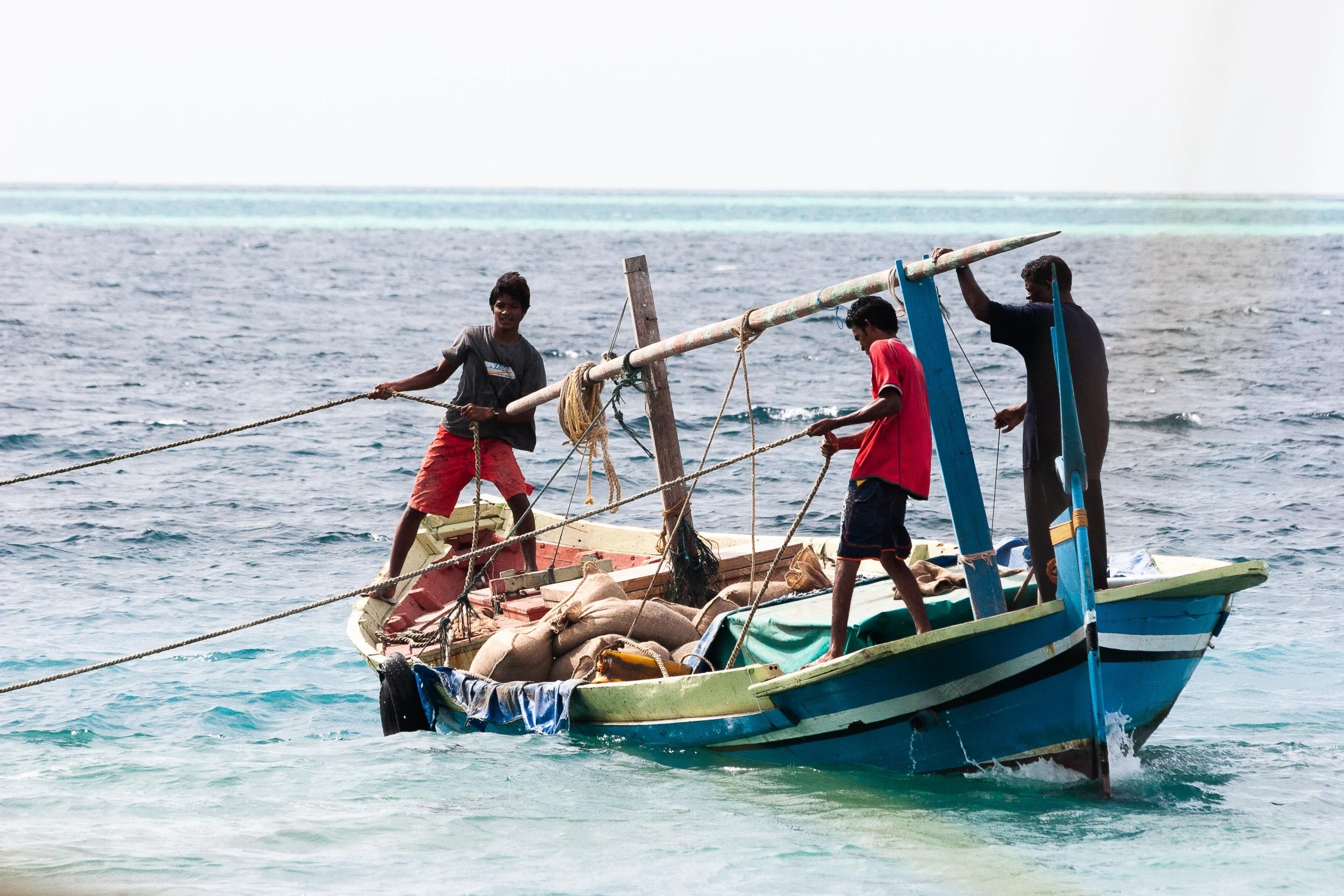 men pulling in a fishing net from the ocean onto a boat
