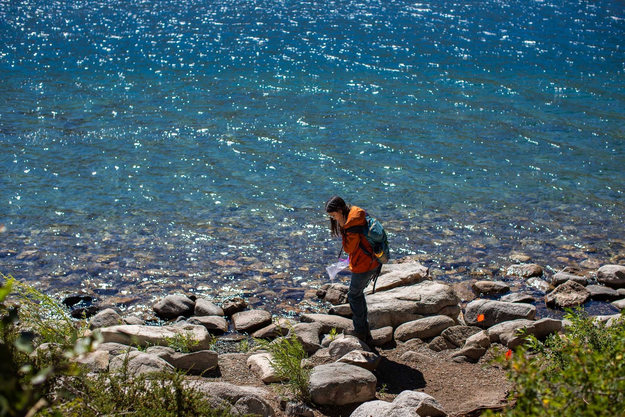 student searching for trash on a rocky lake shore