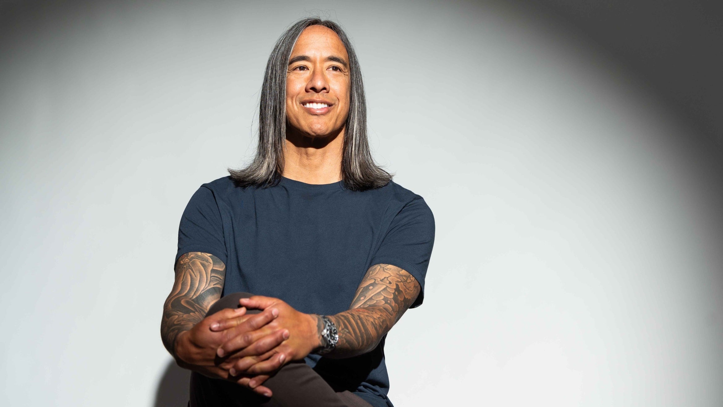 man with grey and black shoulder length hair and tattoos on his arms