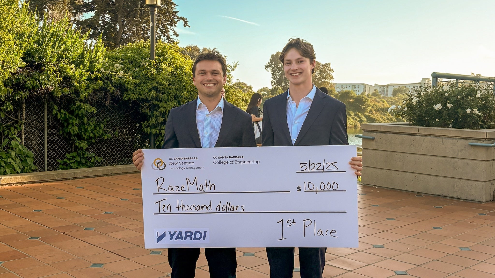 Two young adults wearing suits holding a giant prize check made out to RazeMath
