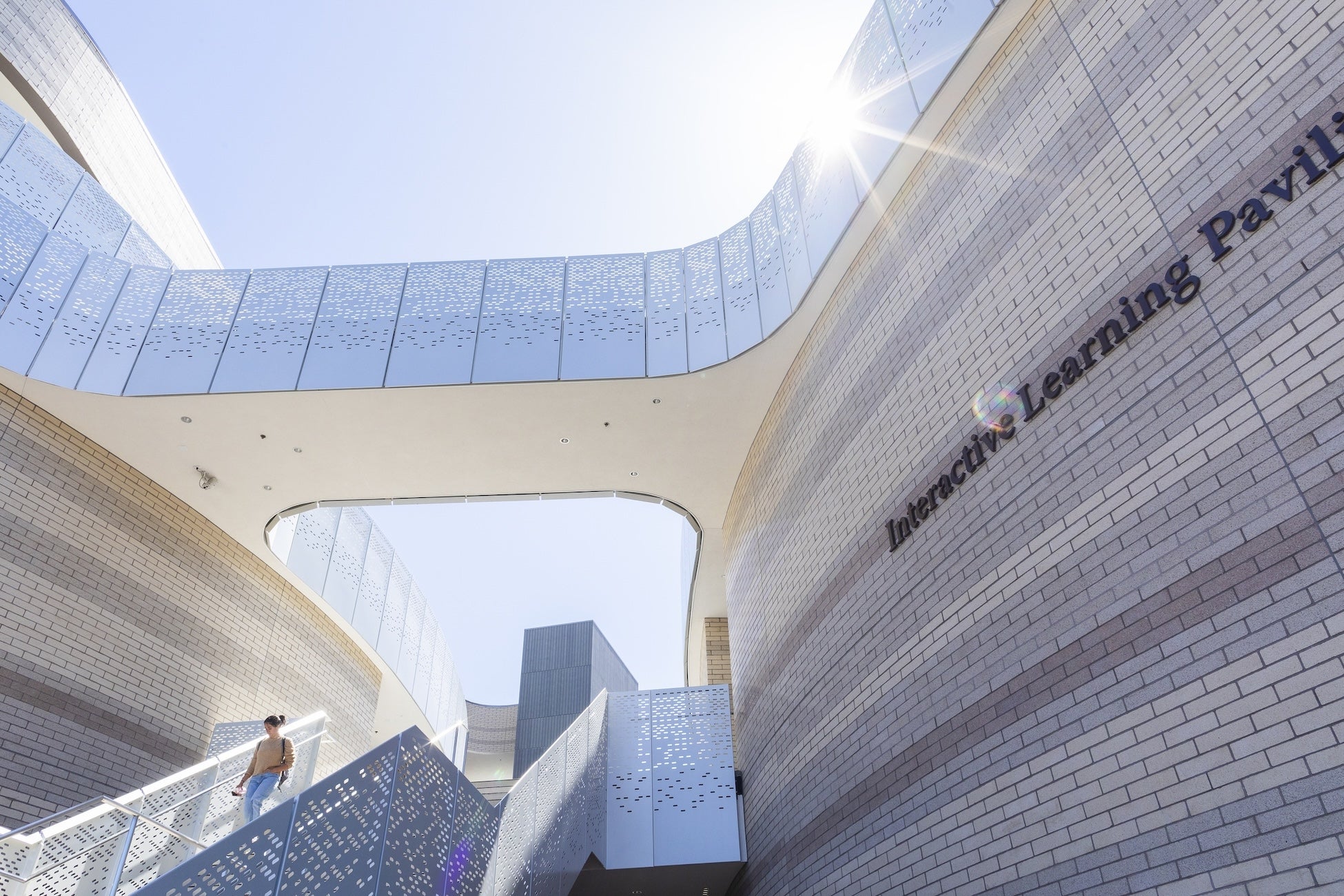 Stairs leading up a modernistic building with a sunburst overhead