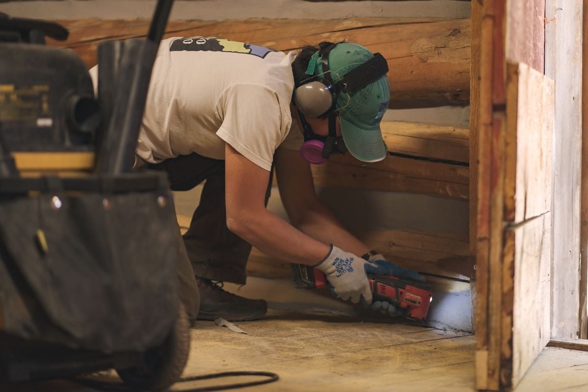 Juyung in PPE works on the floor of a cabin between the door and a shop vac.