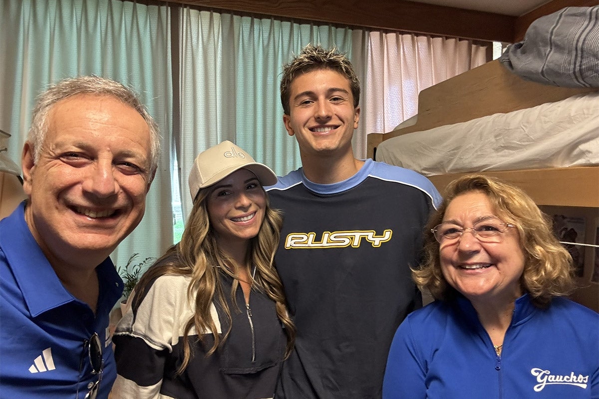 Four adults smiling for a selfie in a college dorm room