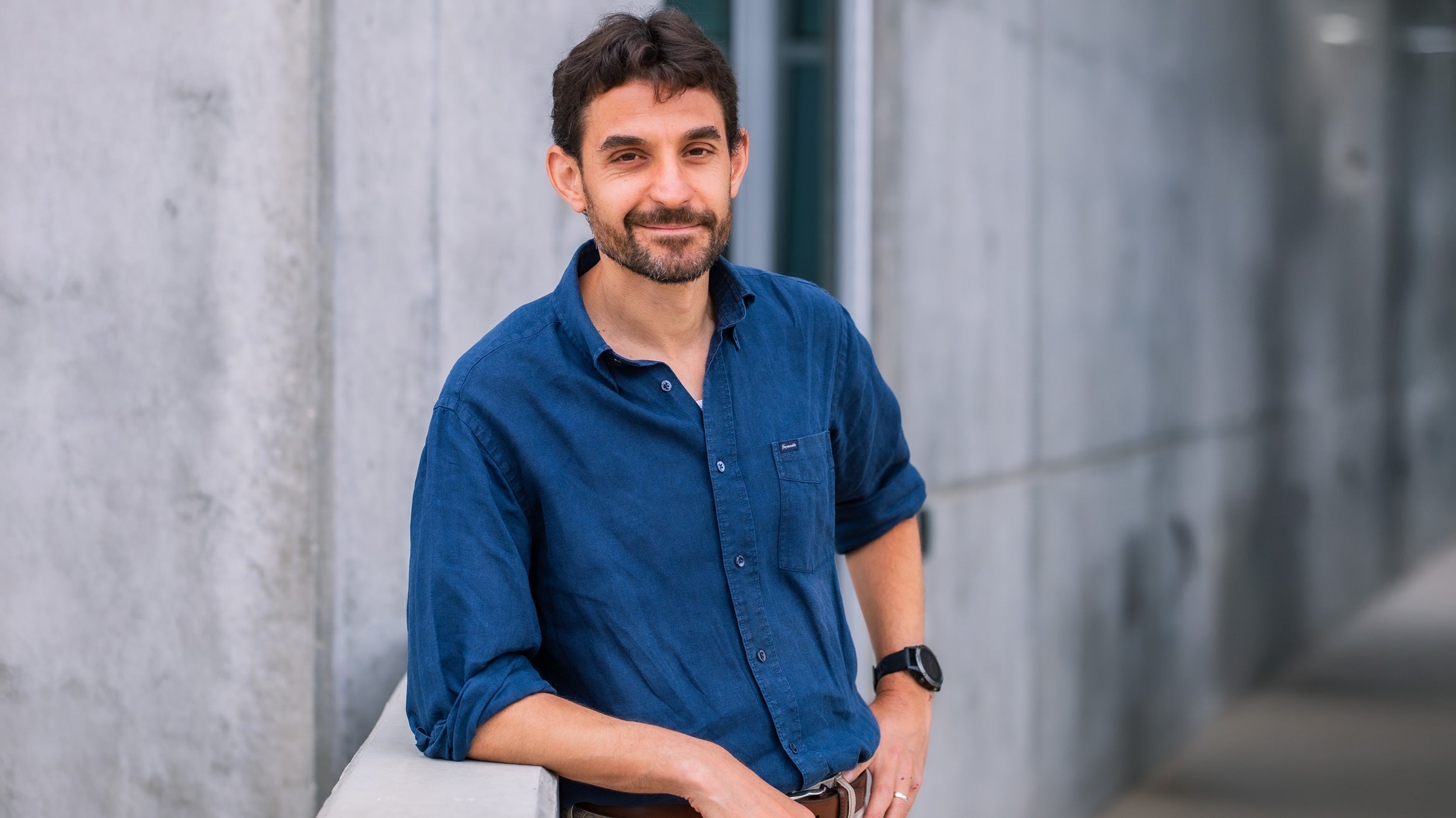 man with beard and watch outside grey concrete building
