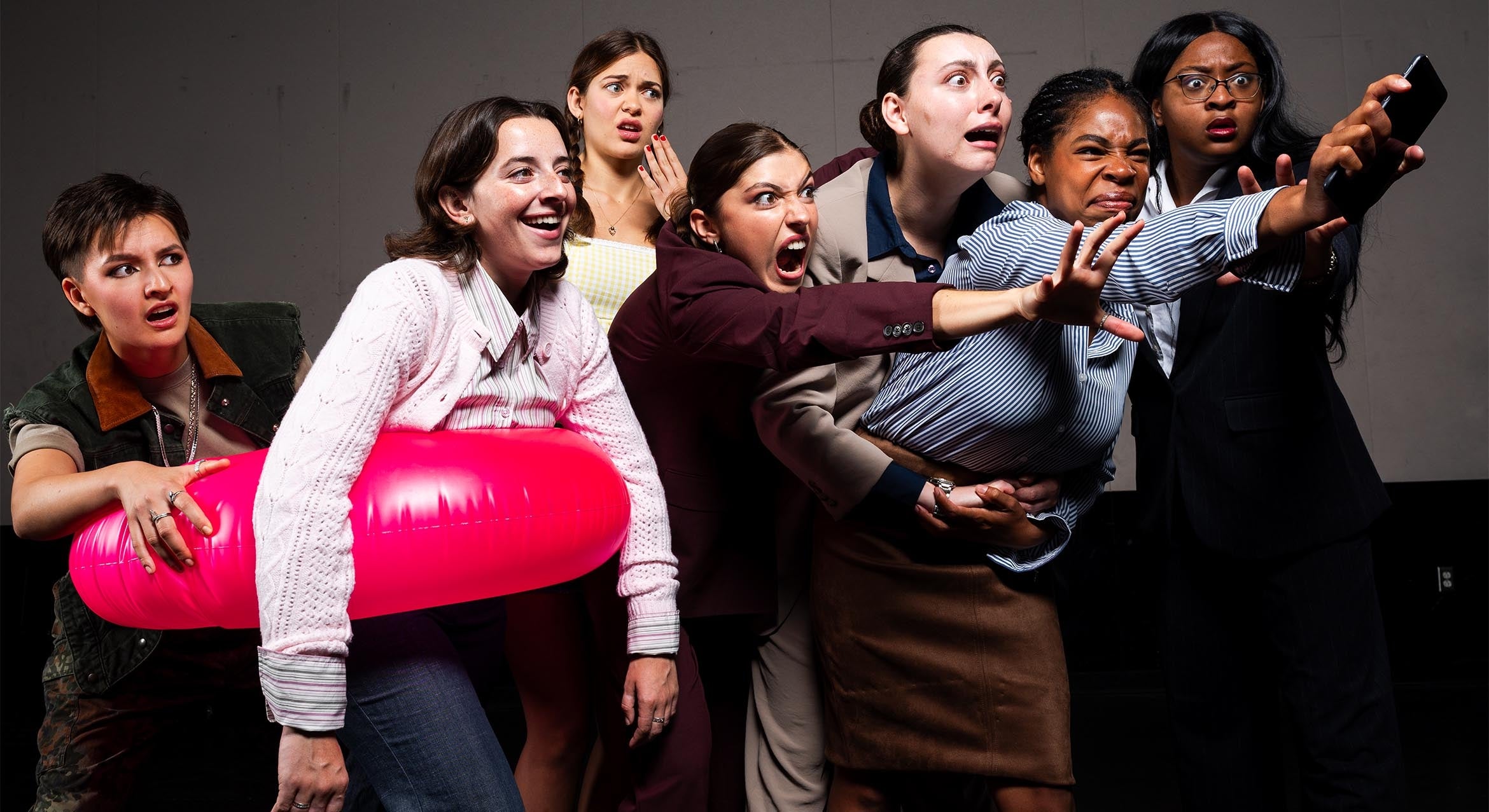 Seven women in business attire stretching the arms forward with the mouths open