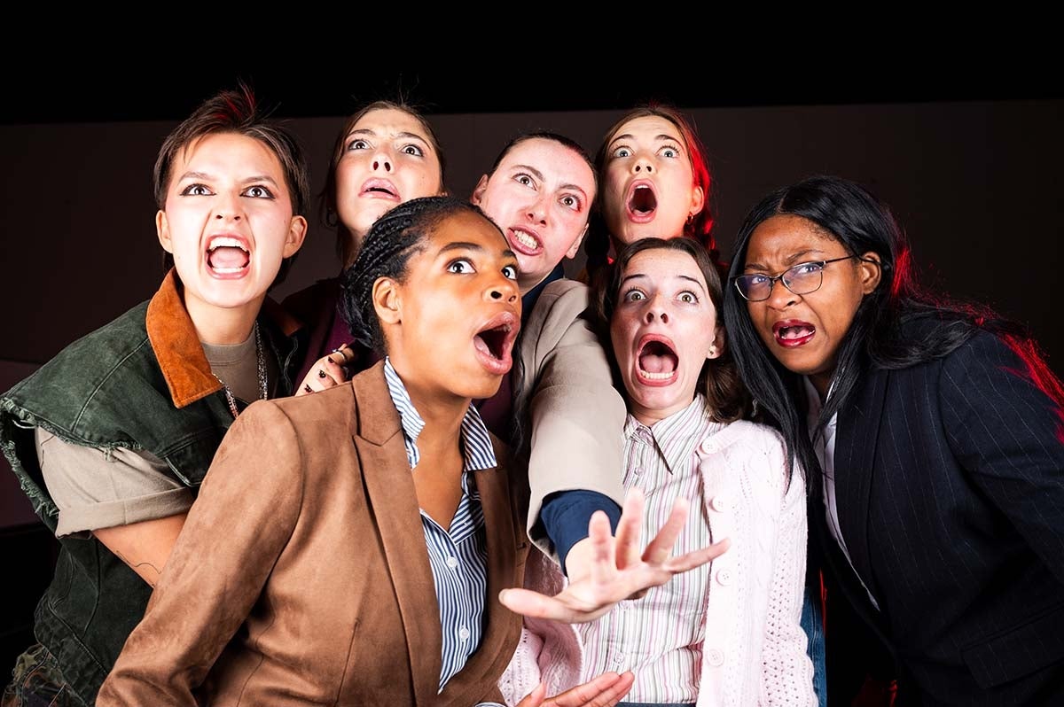 Seven women in business attired with mouths and eyes open in shock