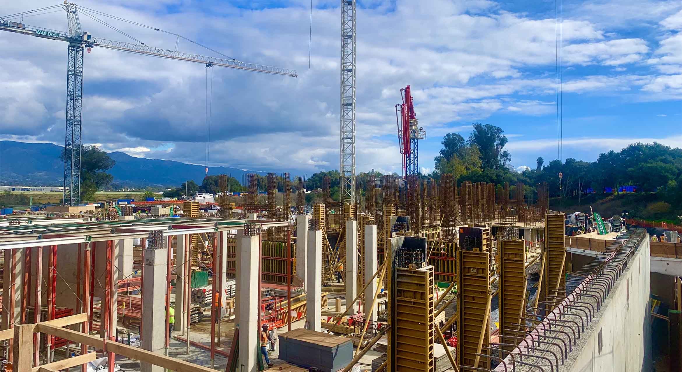 A building under construction. Blue sky and mountains visible behind it.
