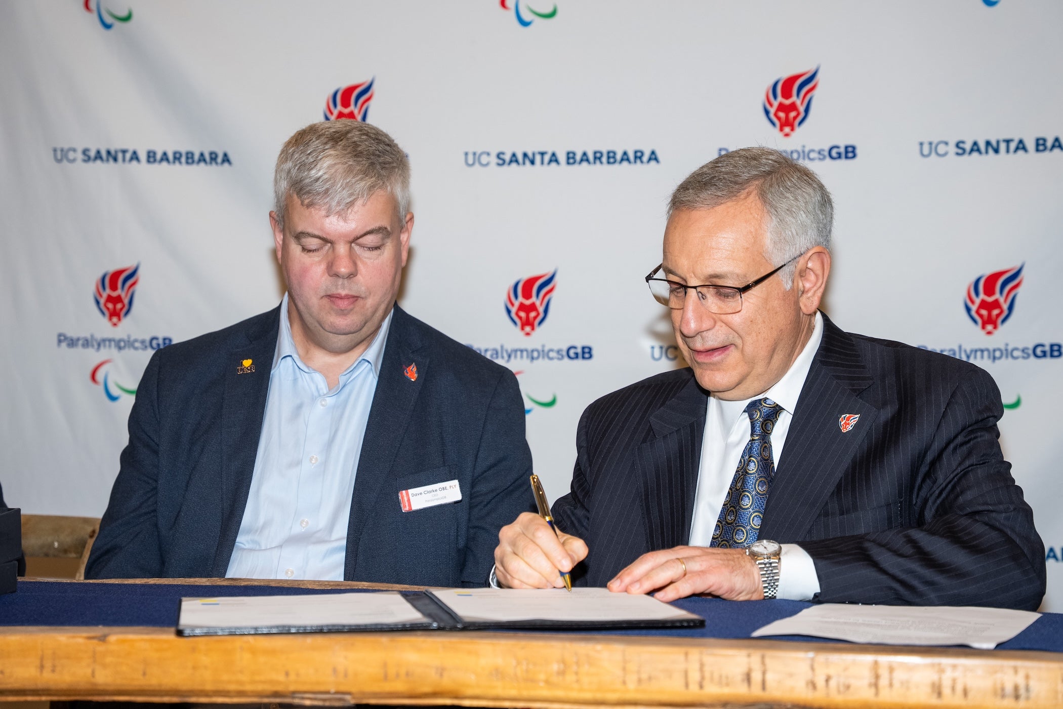 Two men in blue suits looking at a paper that one is signing