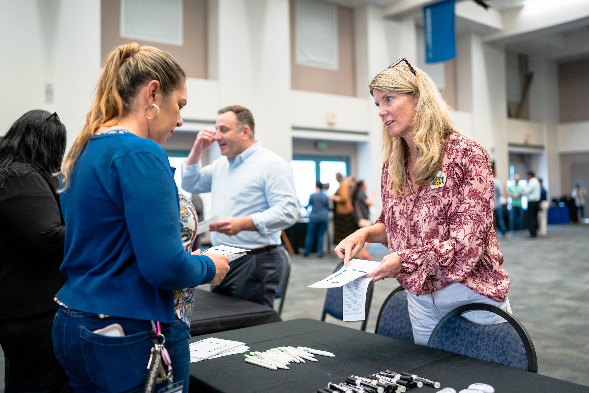 two women discuss financial reporting at a table in a large hall