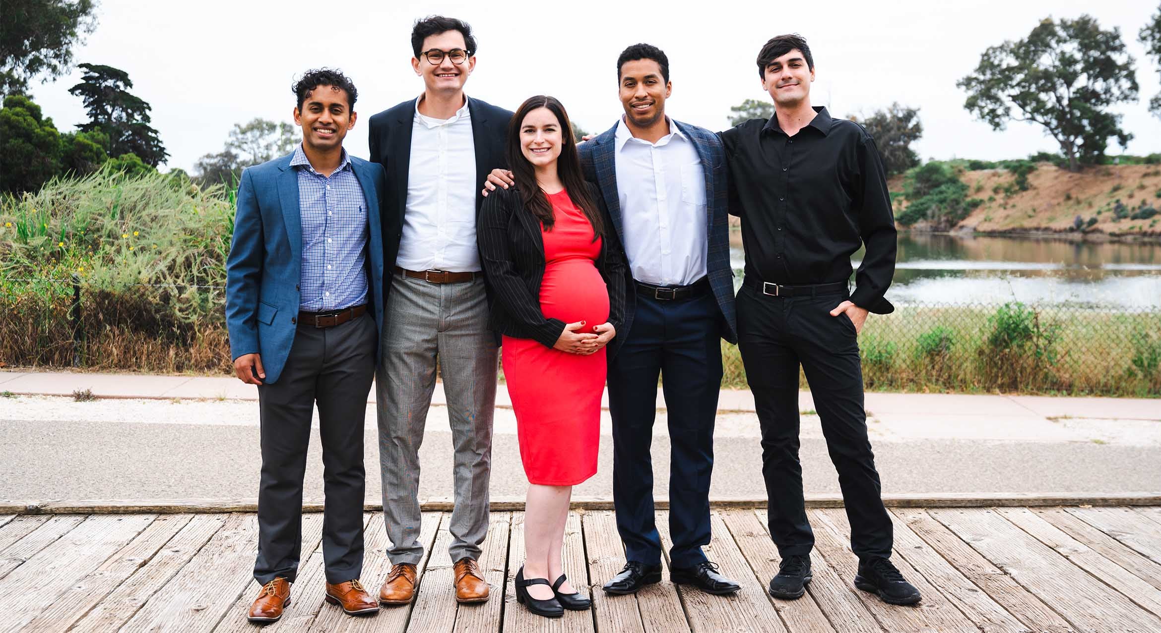 Five adults in business attire standing shoulder to shoulder in a natural setting