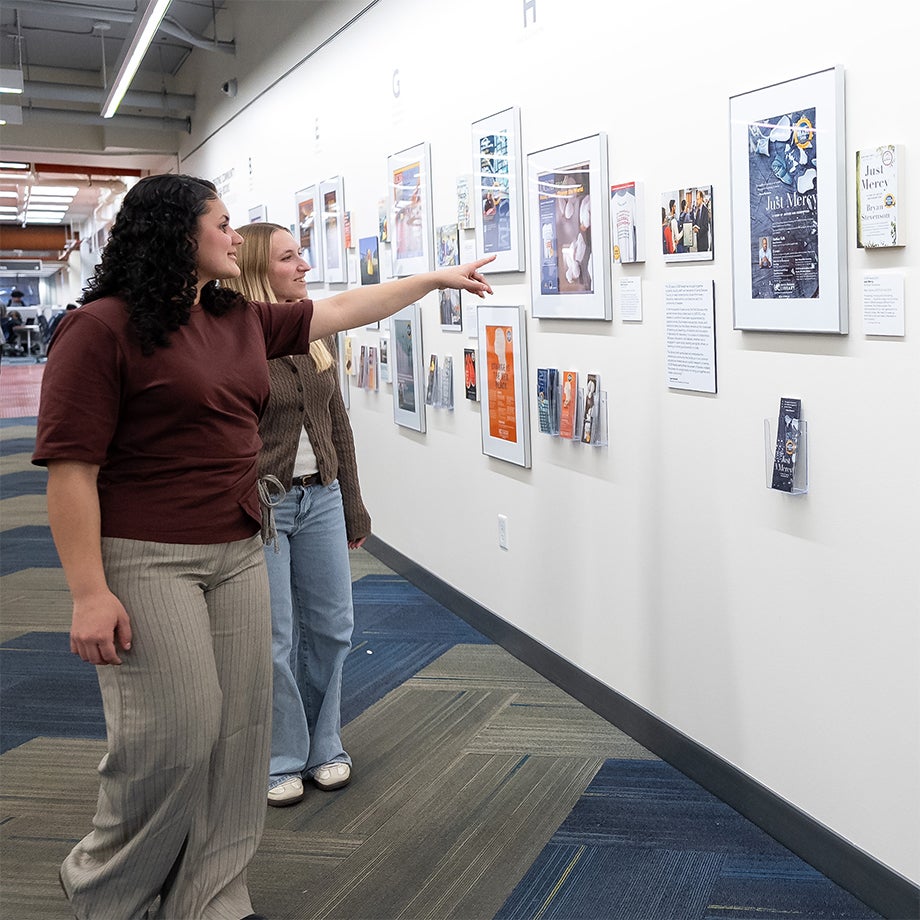 Two women, one pointing toward a framed photograph on a wall