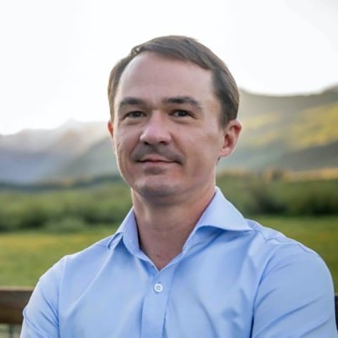 Nathaniel Craig stands outside in a blue shirt with mountains in the distance