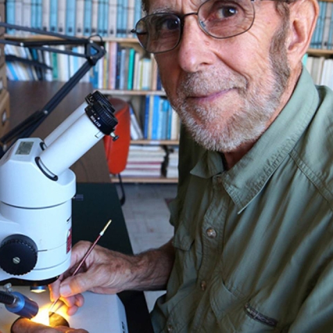 James Kennett sits in front of a microscope