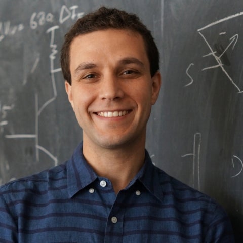 Andrea Young stands in front of a chalkboard wearing a striped blue shirt