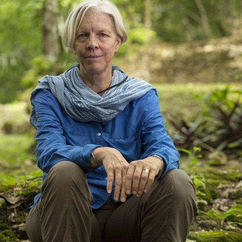 Anabel Ford sits on a log on the jungle floor, wearing a blue top and khaki pants