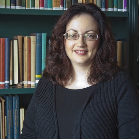 Helen Morales stands in front of a bookshelf wearing a black sweater