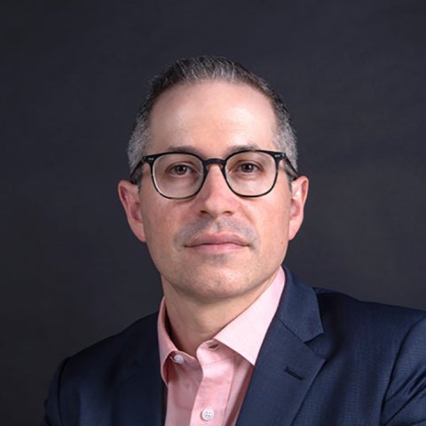 Gabriel Ritter wears glasses and a dark blue blazer over a pink shirt