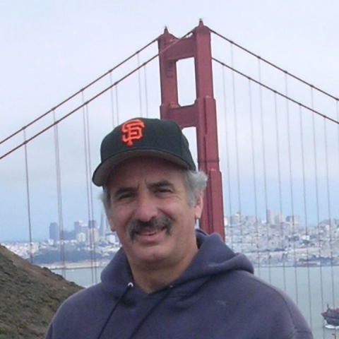 Stuart Feinstein wears a grey sweatshirt and SF Giants hat in front of the Golden Gate Bridge