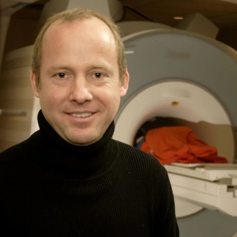 René Weber in a black turtleneck stands in front of an MRI machine