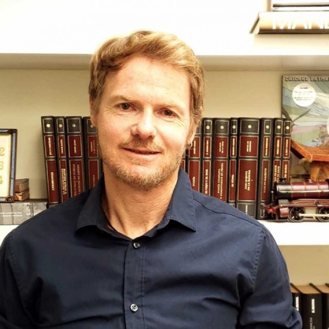 Miguel Eckstein wears a dark shirt standing in front of a bookcase