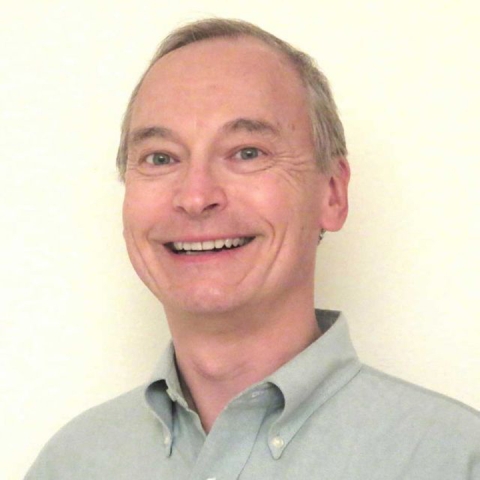 Chris Van De Walle smiles, wearing a grey collared shirt
