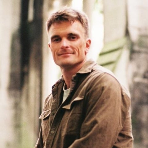 Chase Brewster wears a brown shirt in front of a building