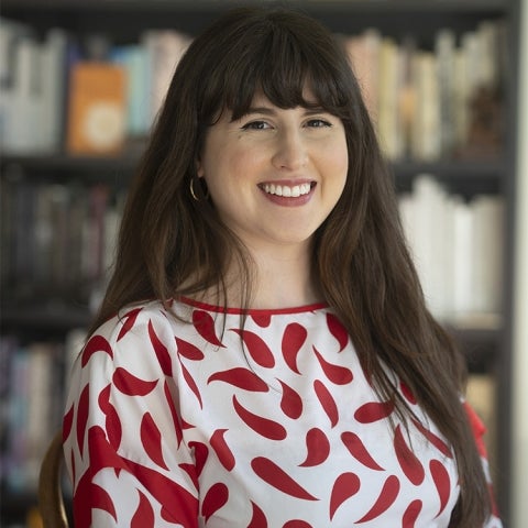 Ana Briz wears a red and white dress while standing in front of a bookshelf