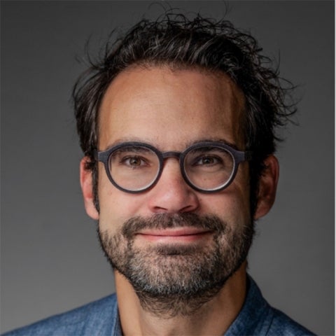 Rafael J.P. Schmitt wears a blue shirt and glasses