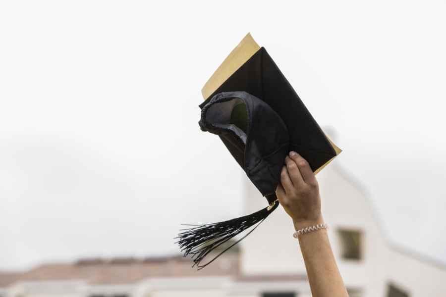 A hand holding a graduation cap and mortarboard into the sky