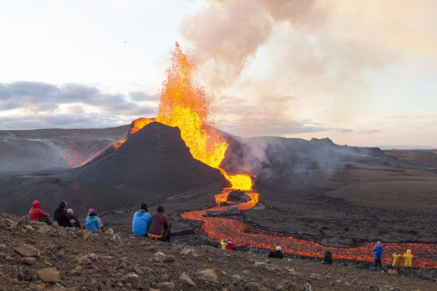 People sit watching erupting volcano in the distance